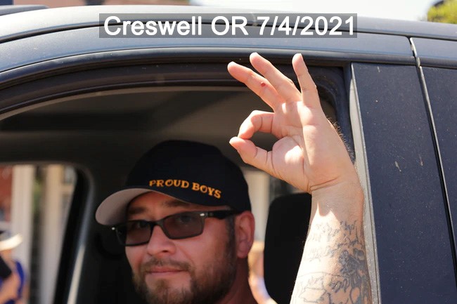 Eric Rogers flashes the OK sign out of a vehicle in Creswell OR. He has an arm tat partially visible. He wears a Proud Boys hat. 