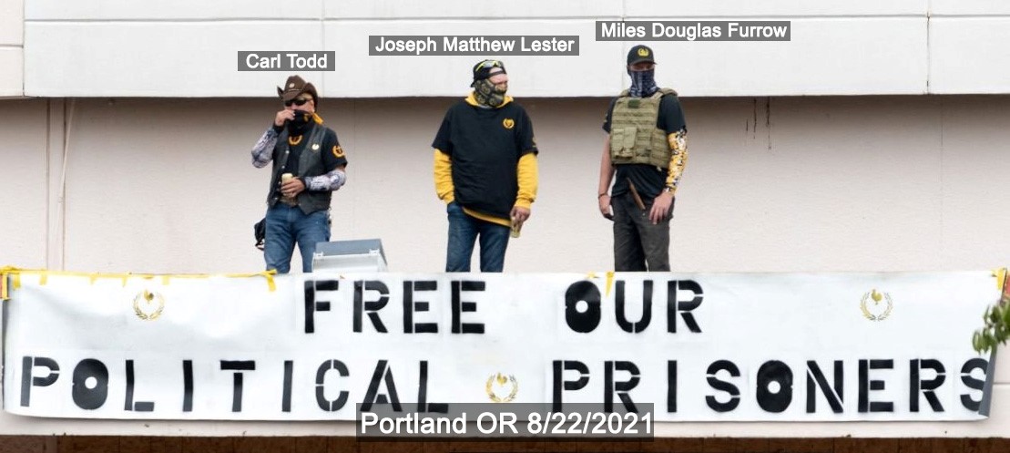 Joey Lester and two other proud boys stand on a roof. A badly made banner says "free our political prisoners."