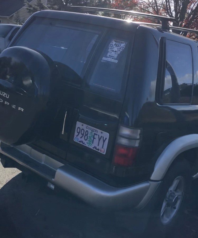 photo of a black vehicle with oregon plate 998 fyy and a checkered past sticker on the back window. Photo is taken from behind the vehicle. 